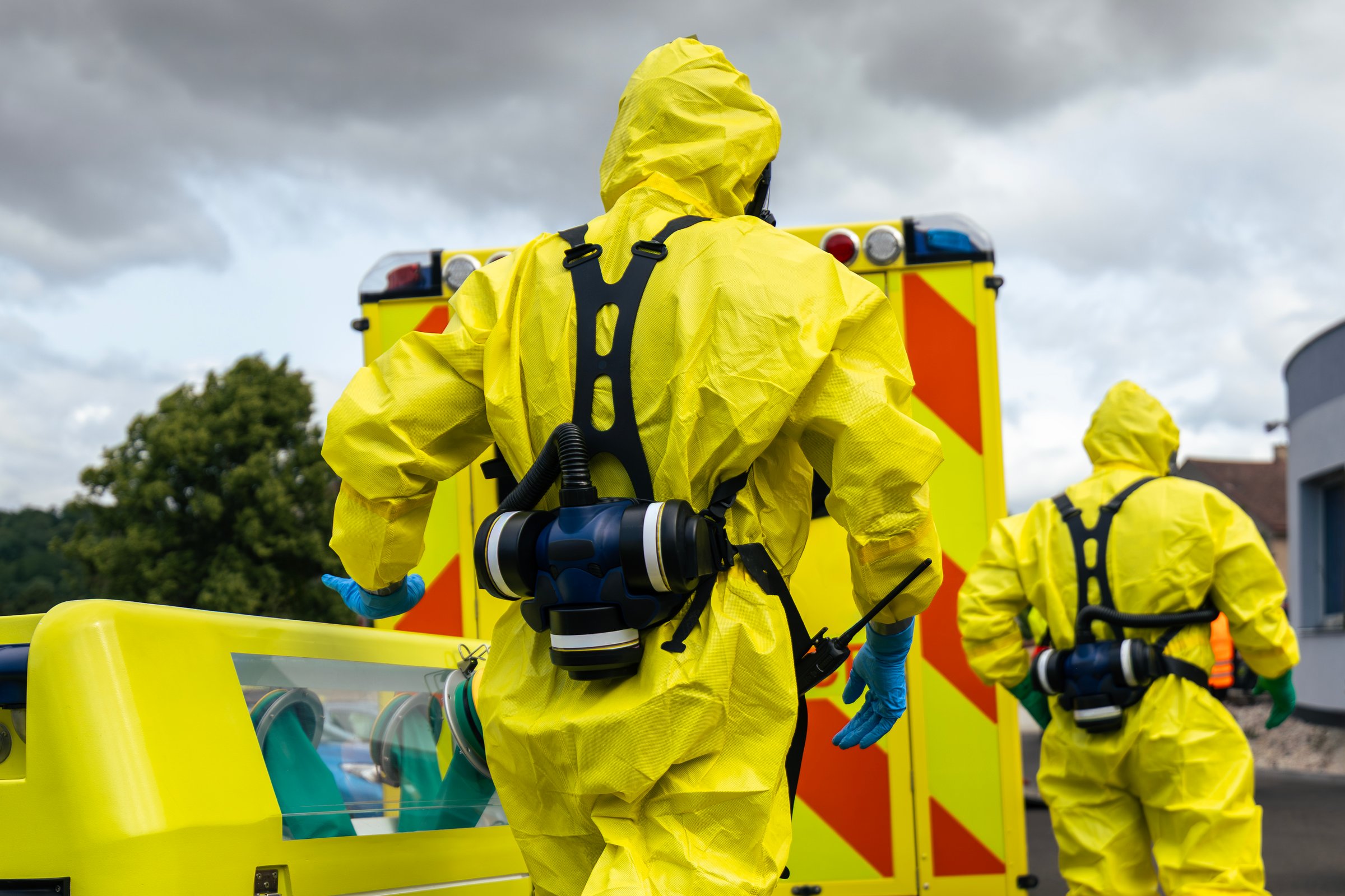 Members of biohazard team of emergency medical service in protective suit against ambulance during training.