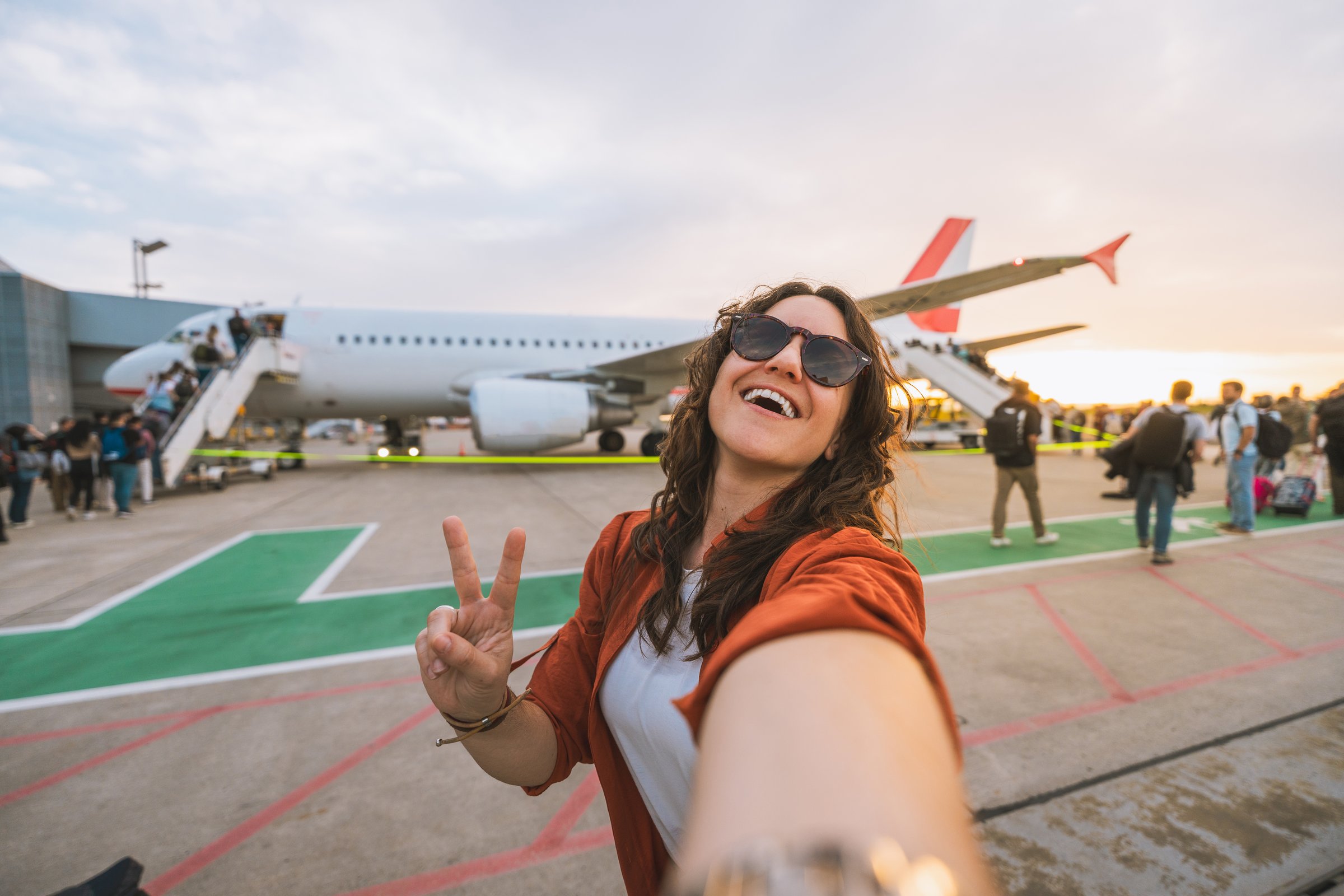 Smiling woman taking selfie at airport runway before boarding. Concept: travel, airplane journey, holiday, freedom, summer escape.