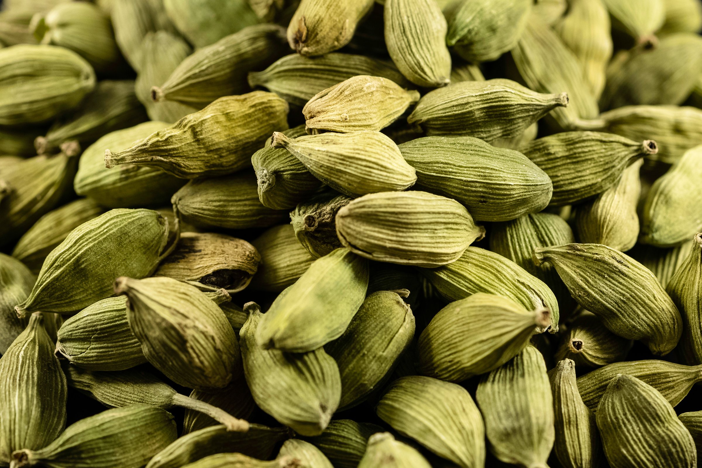 Close-up of a pile of green cardamom pods, showcasing their ridged texture and natural green color.