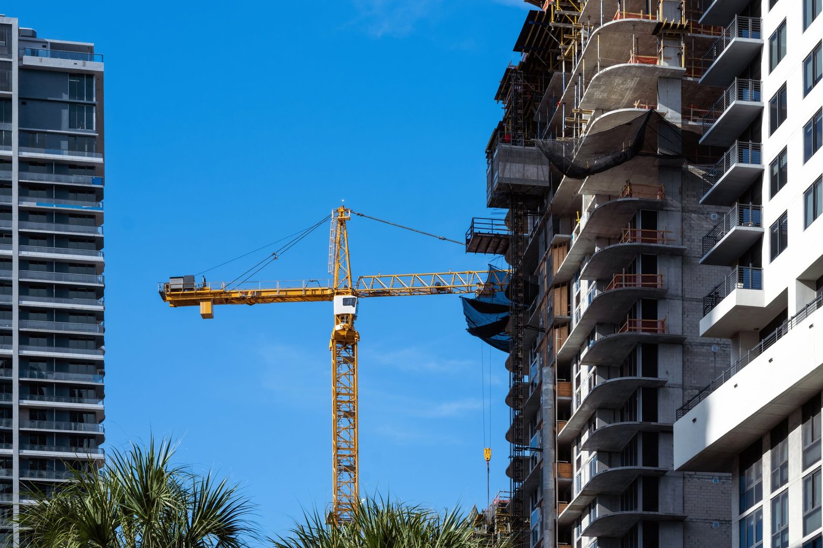 Cranes at skyscraper construction site with buildings and blue sky behind it