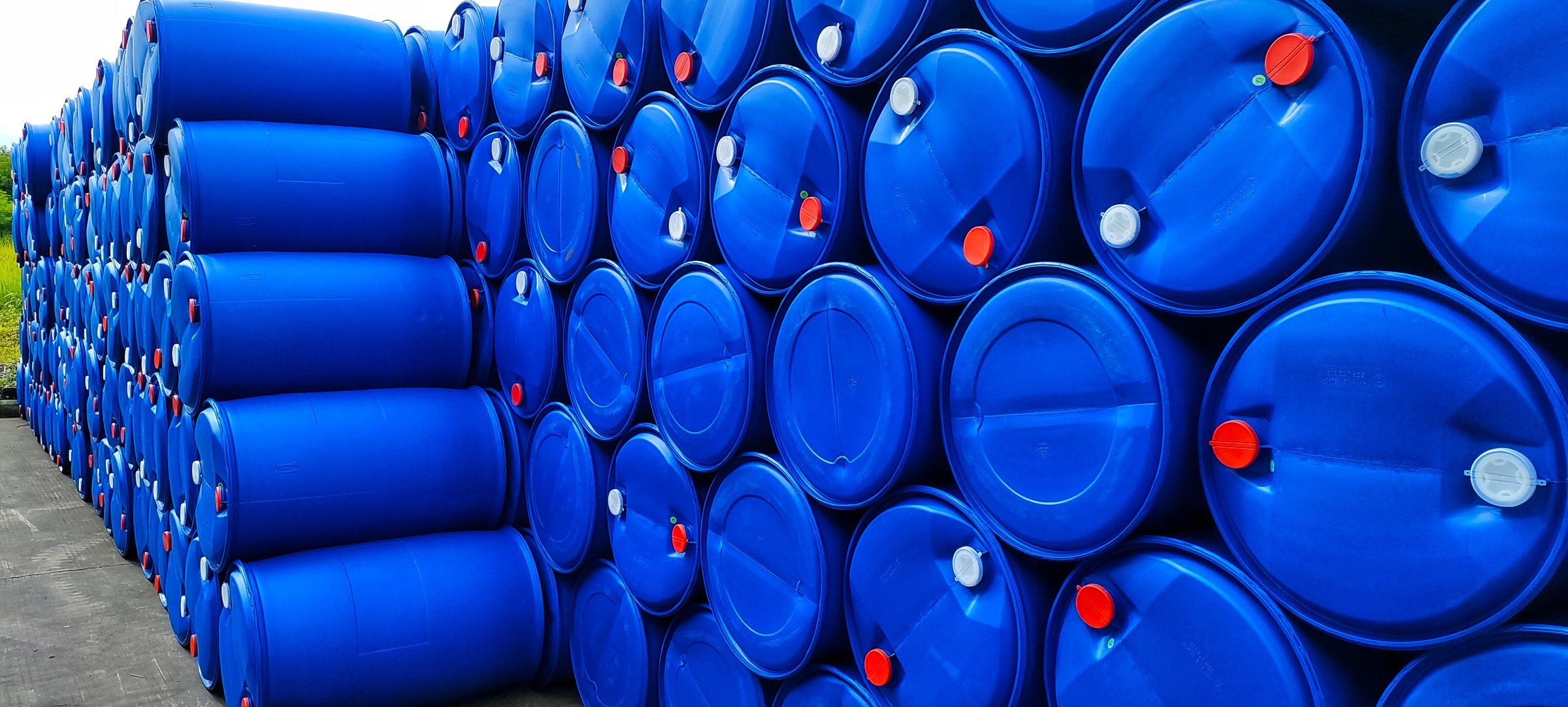 Two rows of plastic chemical drums stack in outdoor warehouse