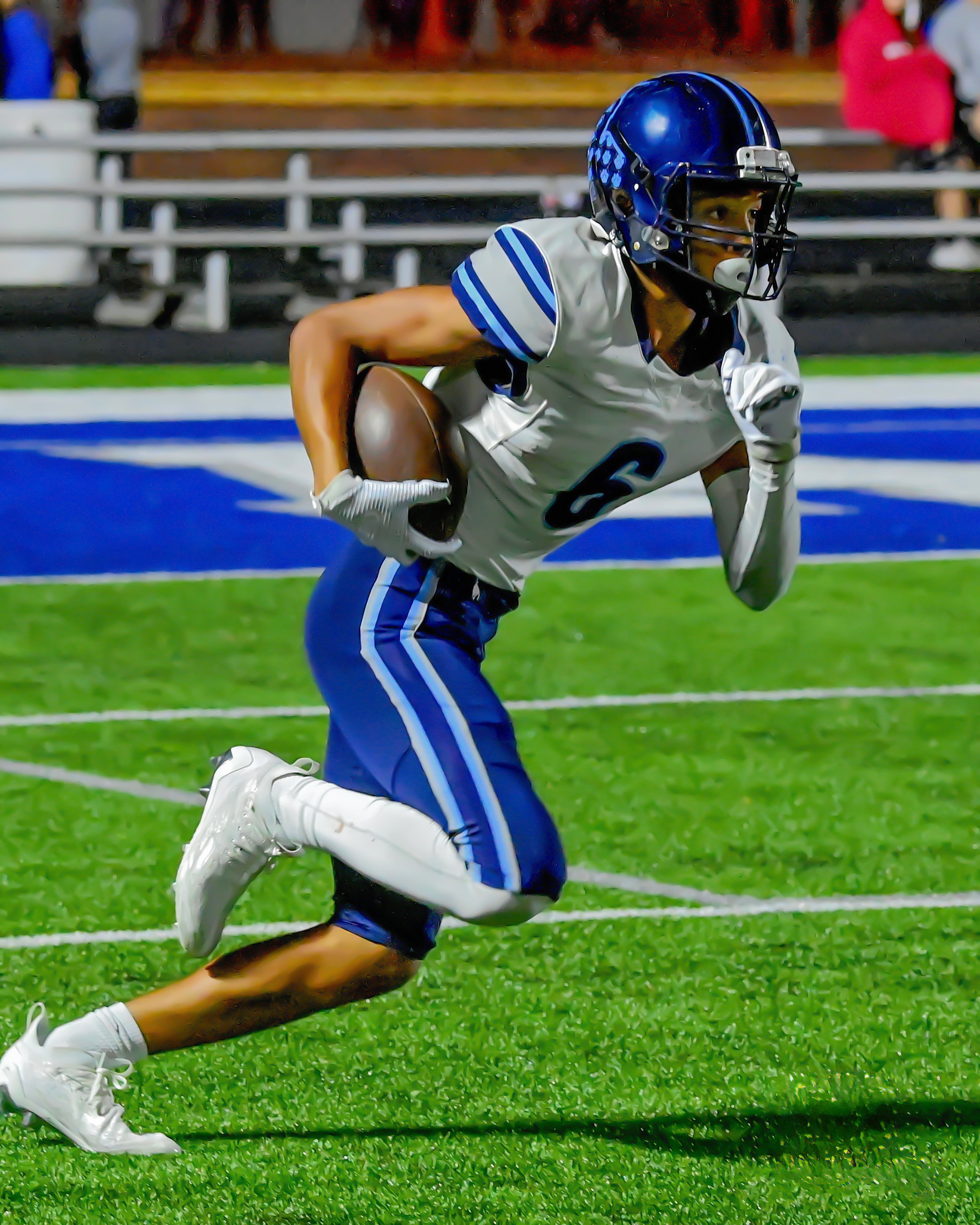 Teenage football player heading up field with the ball under his arm as he returns the kickoff.