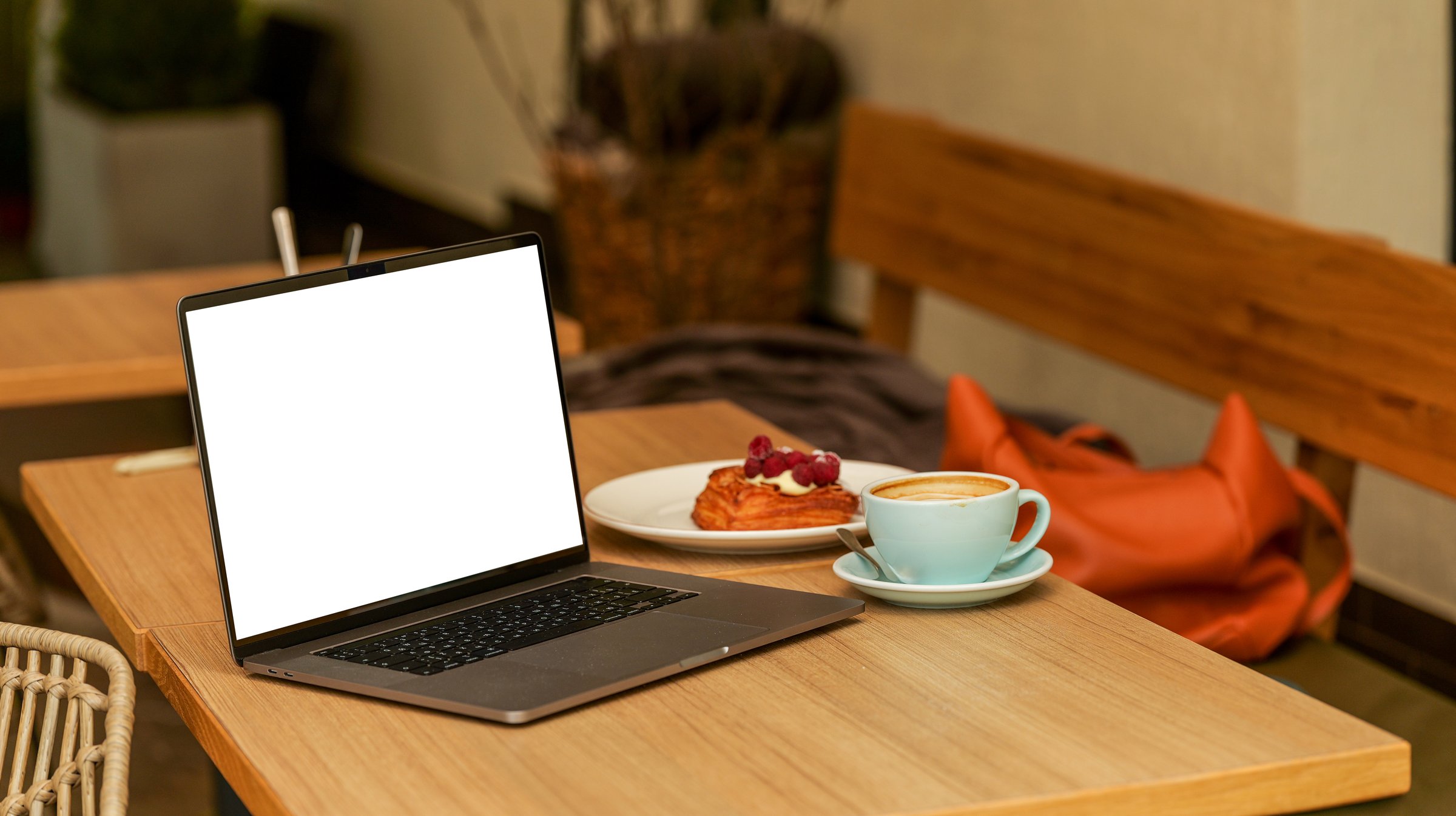 A laptop sits on a wooden table next to a cup of coffee and a pastry, perfect for remote work or studying