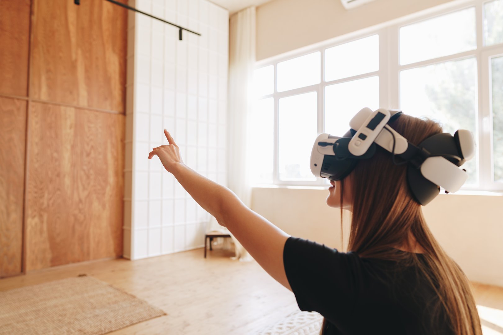 In a modern indoor environment, a woman wearing a virtual reality headset enthusiastically interacts with a virtual world, pointing towards an unseen object while enjoying the immersive experience.