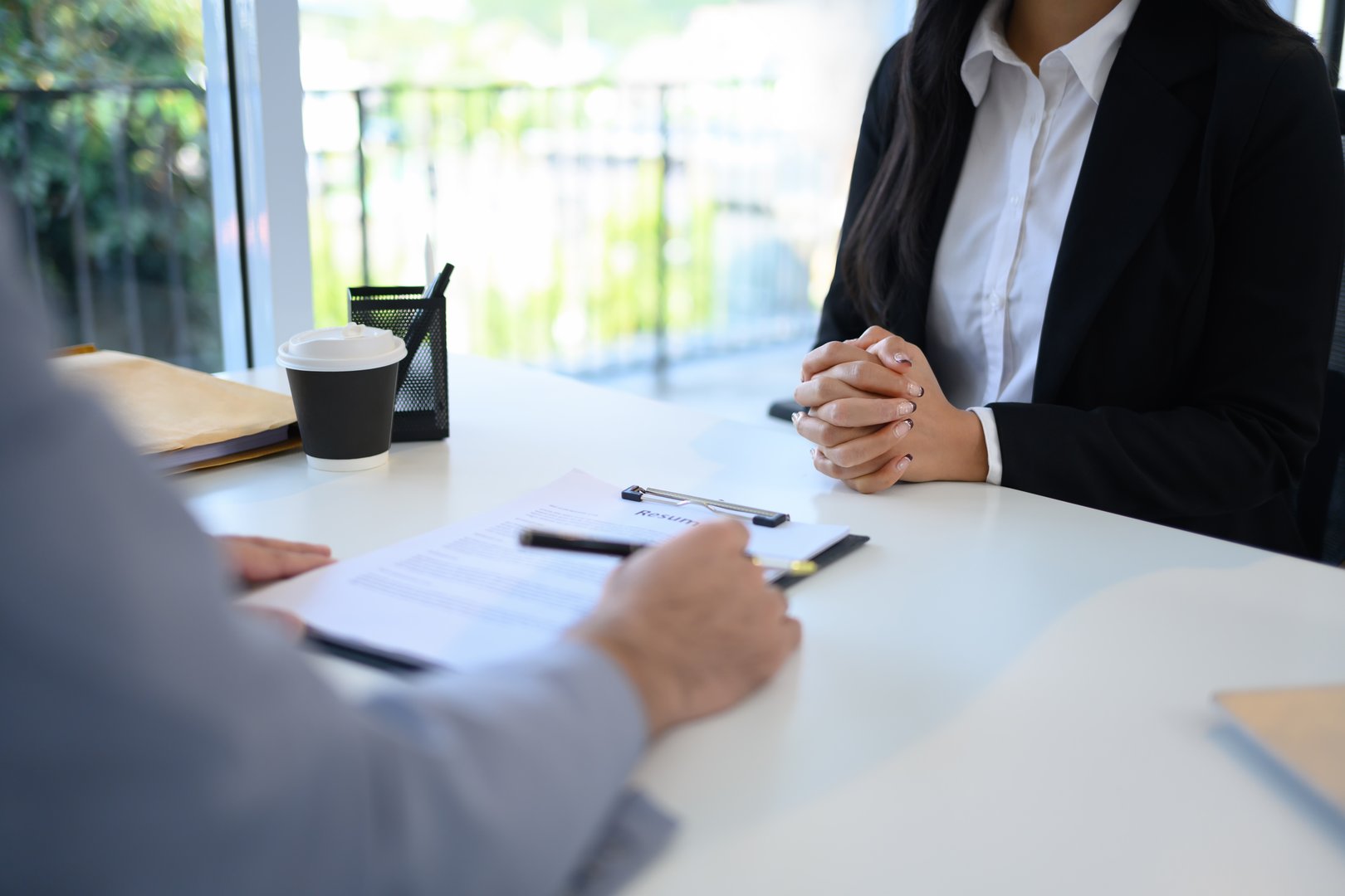 Candidate in formal wears attentively sitting across from an interviewer reviewing her resume.
