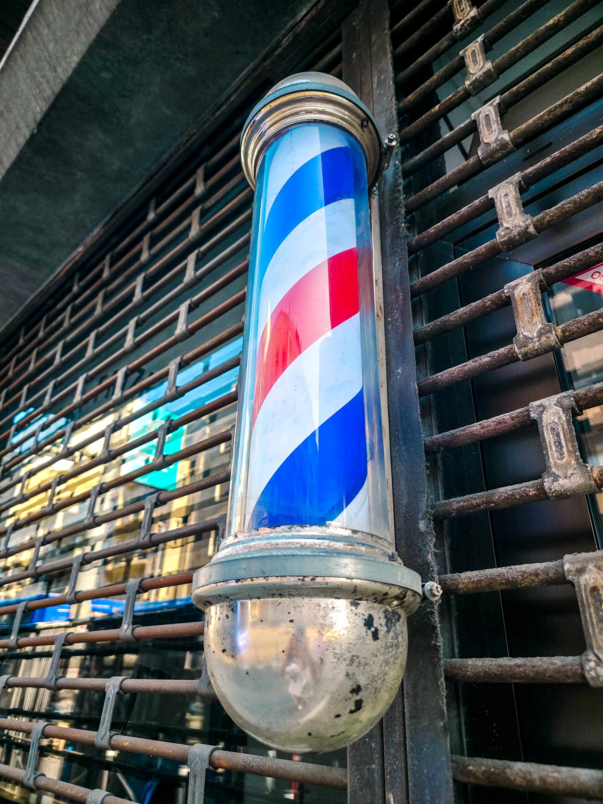 Close-up of traditional barber pole in Belgrade. Red, white, and blue spiral stripes on a vintage metallic fixture, symbol of classic barbershop culture and urban street style.