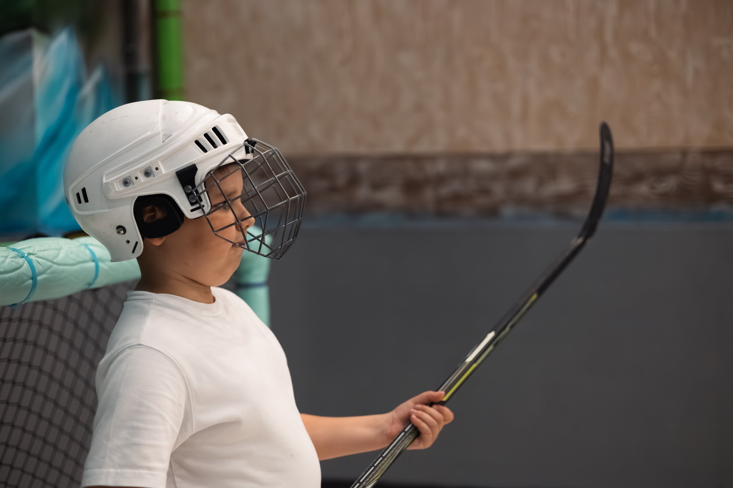 A boy wearing a protective hockey helmet holds a hockey stick during training, developing skills and passion for the sport. A teenager stands in a protective helmet and holds a hockey stick in a goal.