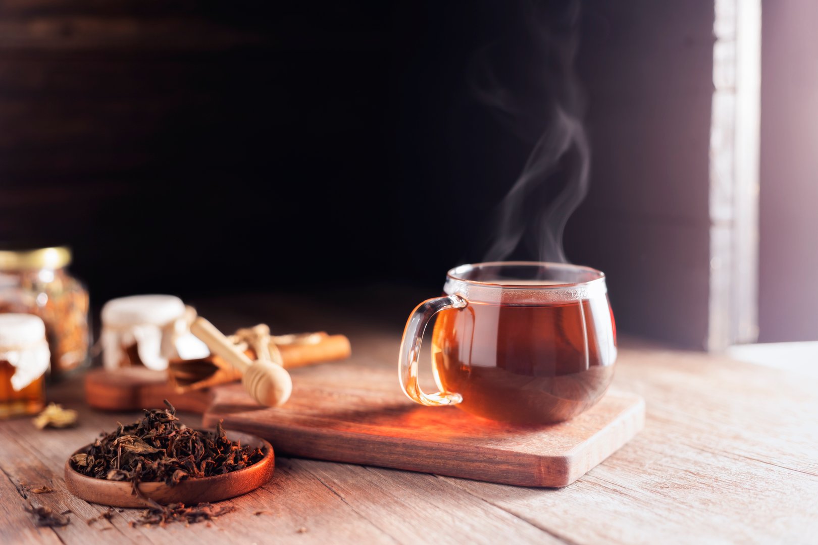 Cup or tea glass Hot brew and dried tea leaves on a wooden plate, placed on a wooden table, on a dark black background.