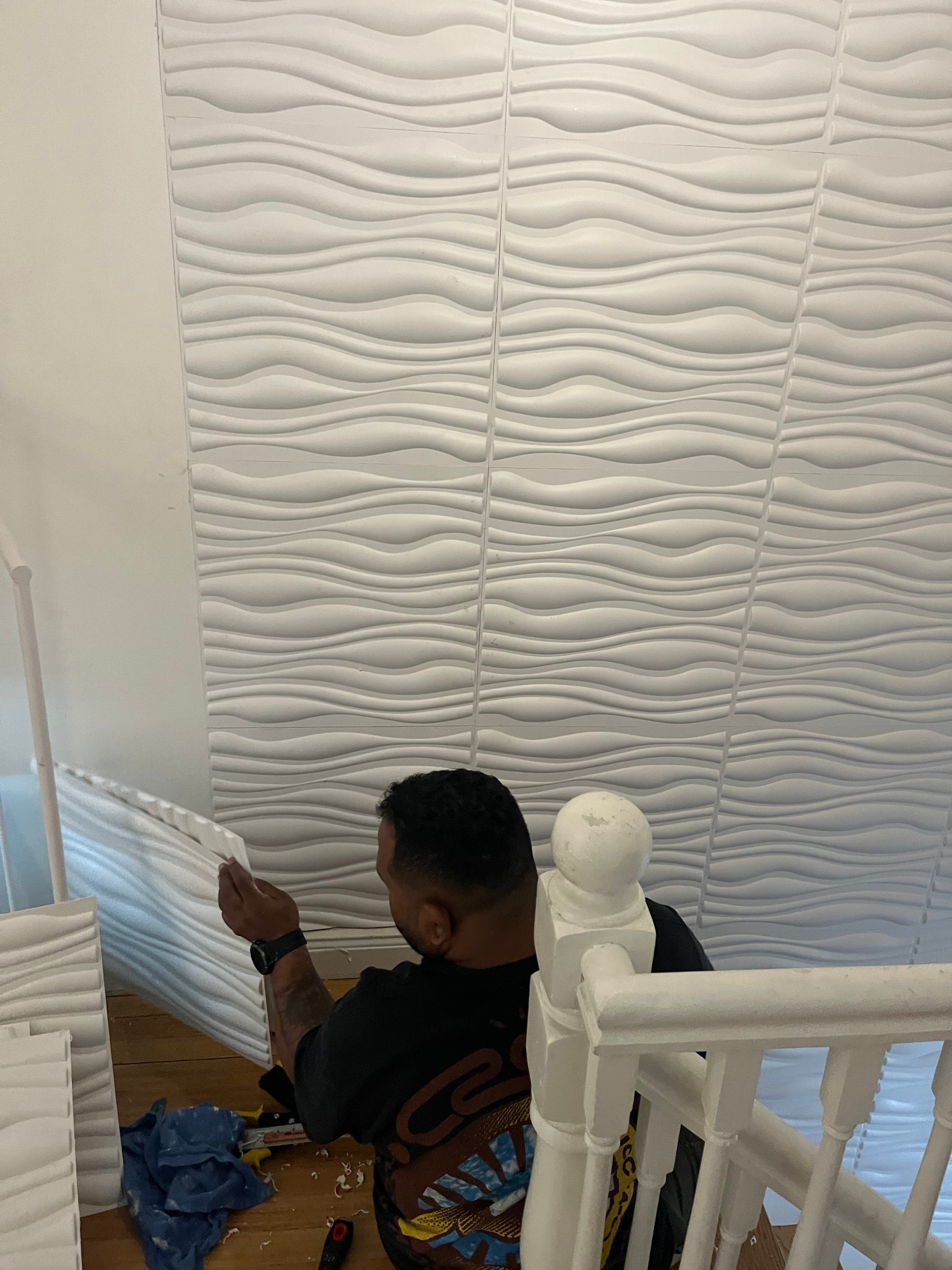 Person installing decorative white wave-patterned wall panels on a stairwell.
