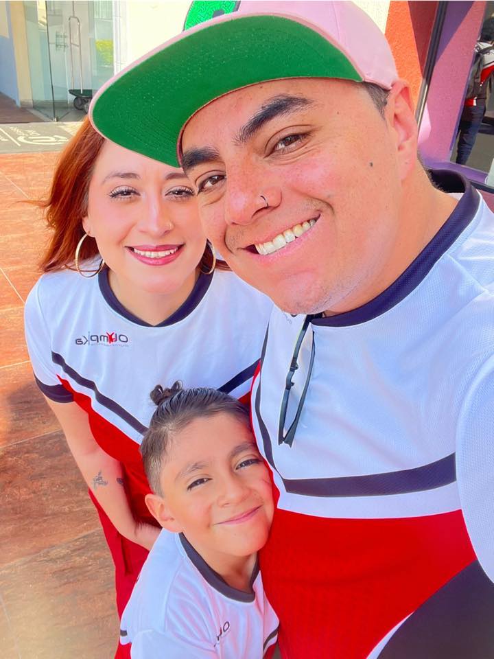 Smiling family wearing matching outfits, father with a pink cap, mother and child in coordinated shirts, posing outdoors.