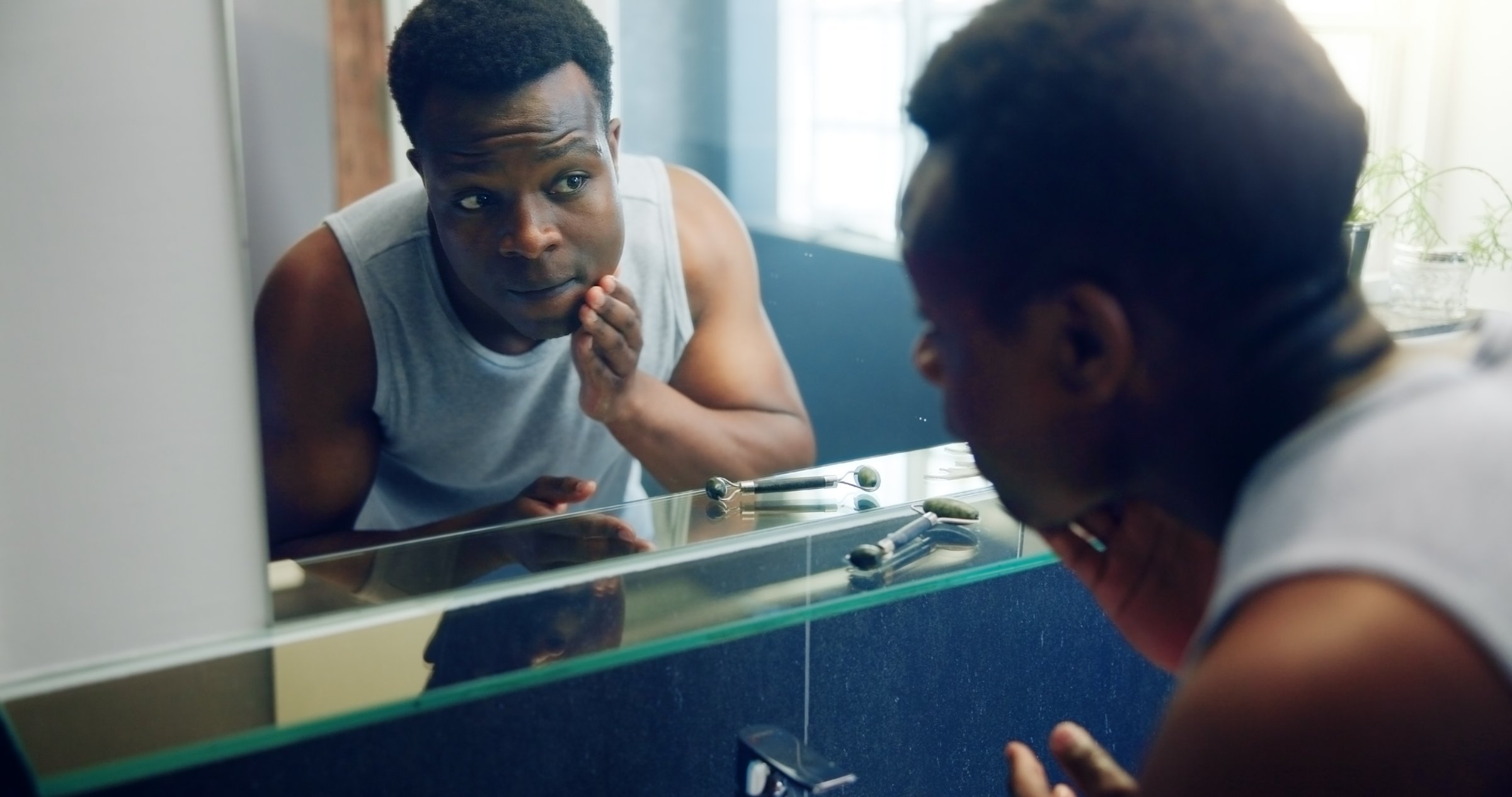 African man, bathroom mirror and inspection for skin with results, reflection and shaving with grooming in home. Person, glow and facial change in morning with thinking, hygiene or cosmetics at house