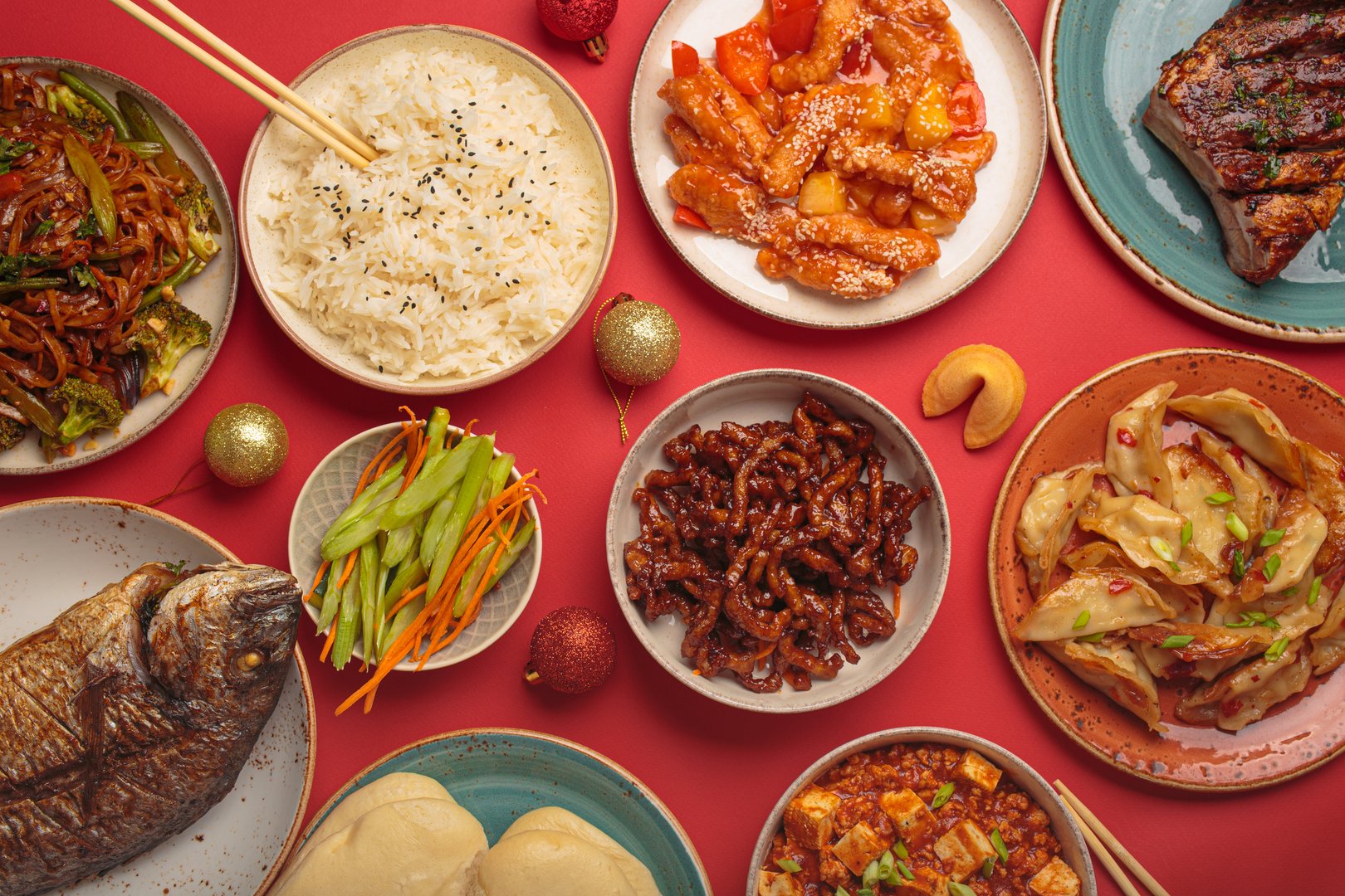 Vibrant chinese new year traditional dishes on a festive red background: kung pal chicken, sweet and sour pork, noodles, dumplings, mapo tofu, fish, rice, fortune cookies. Copy space