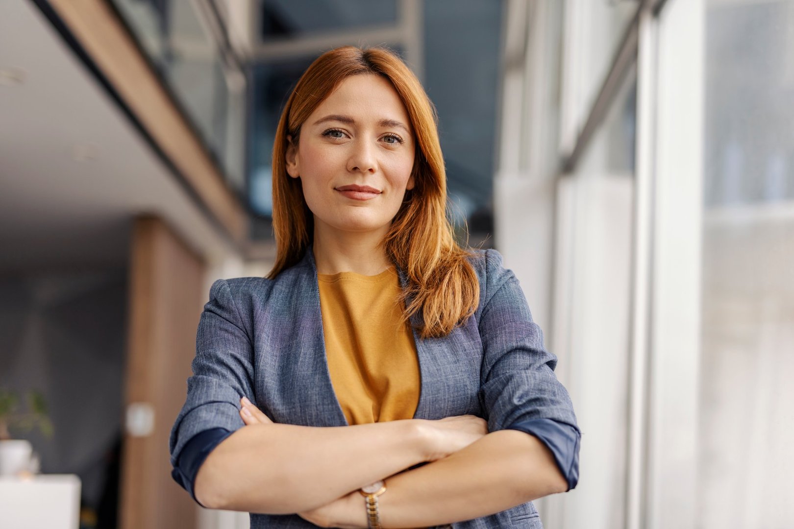 Portrait of female leader standing at corporate firm with arms crossed and smiling at camera.
