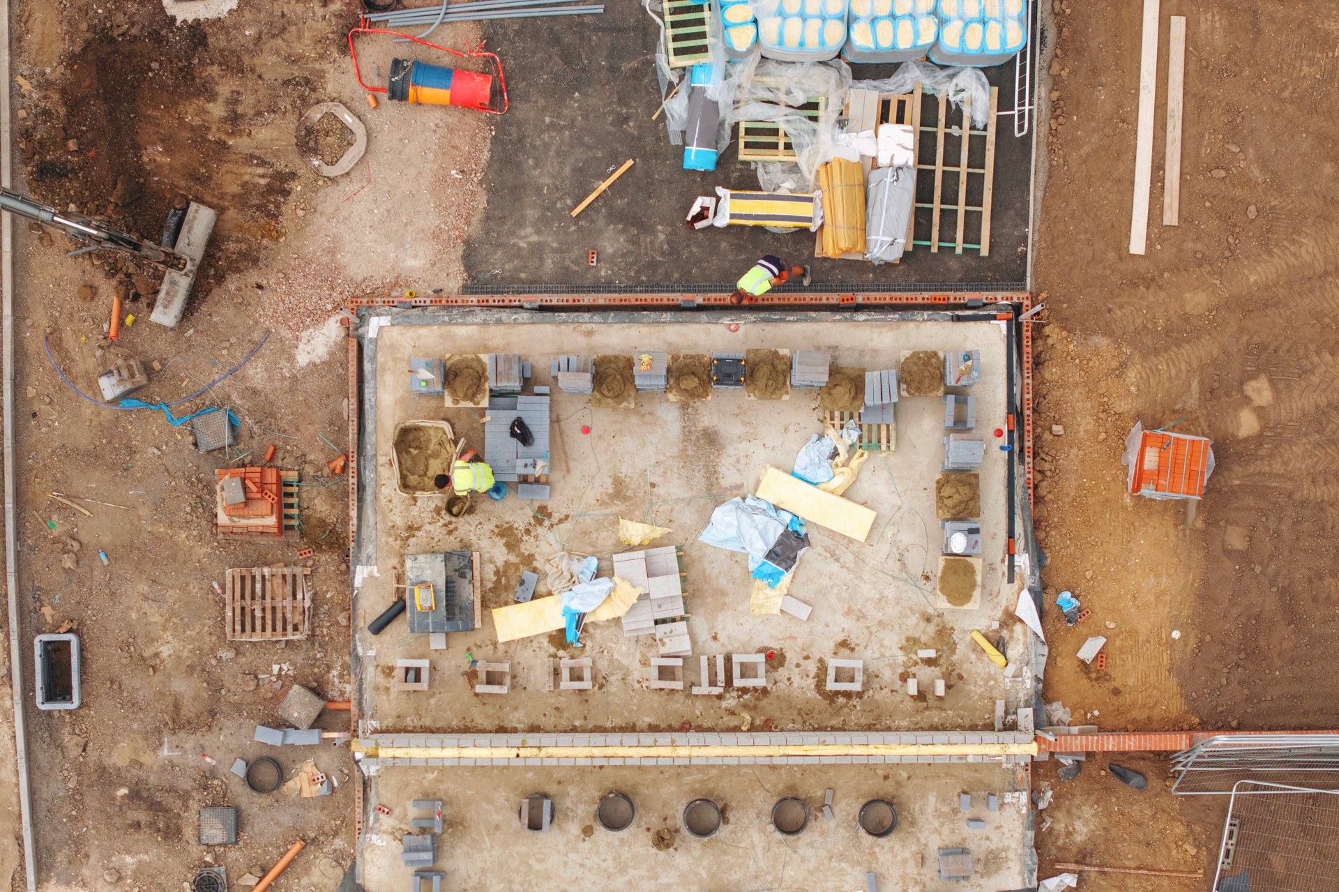 Workers actively preparing construction site with foundations and organized materials