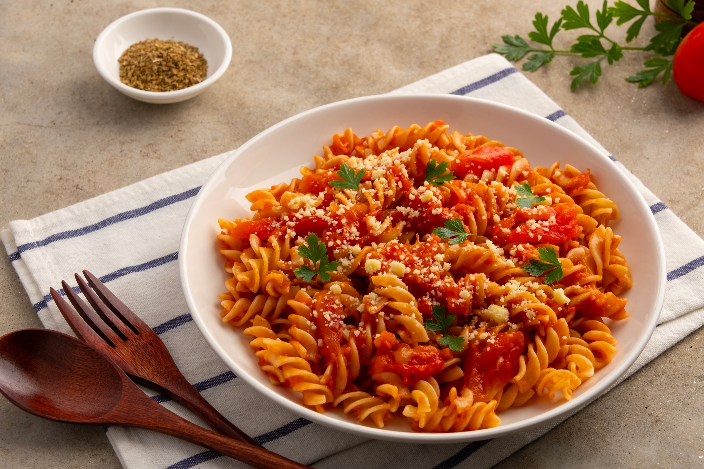 Fusilli macaroni with fresh tomatoes sauce in white plate.topped with parmesan cheese and parsley.