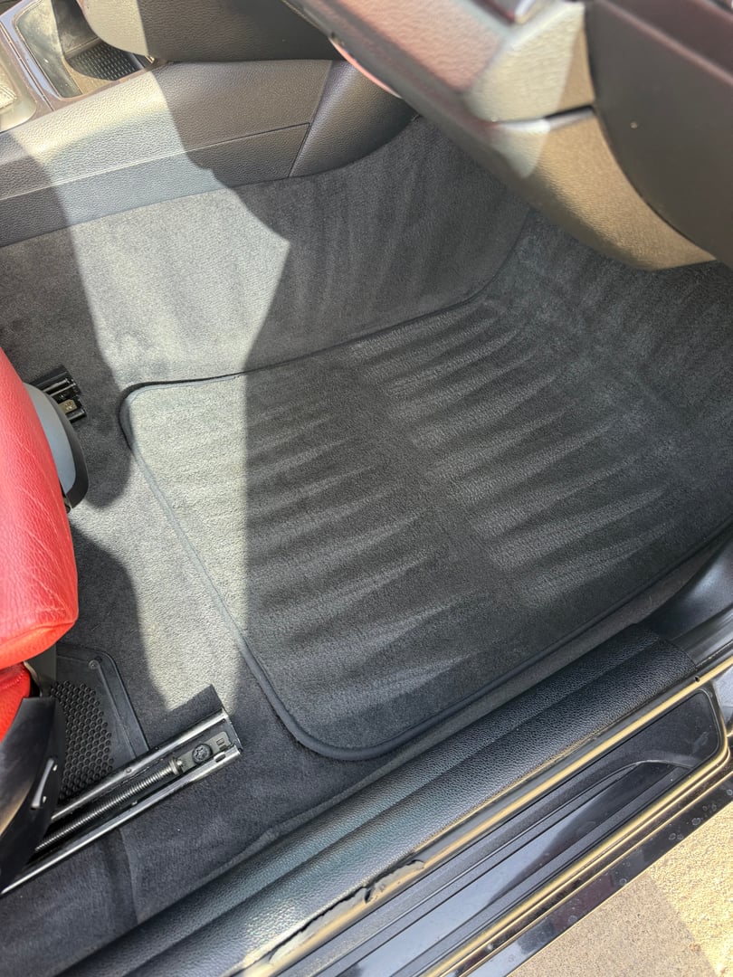 Car interior showing a black floor mat and a red leather seat.