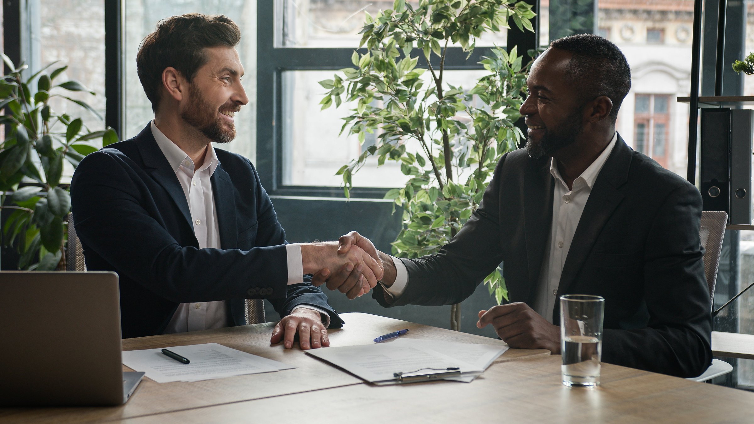 Two diverse multiracial businessmen Caucasian man and African American businessman partners men signing contract agreement document shaking hands conclude success business deal partnership in office. High quality 4k footage