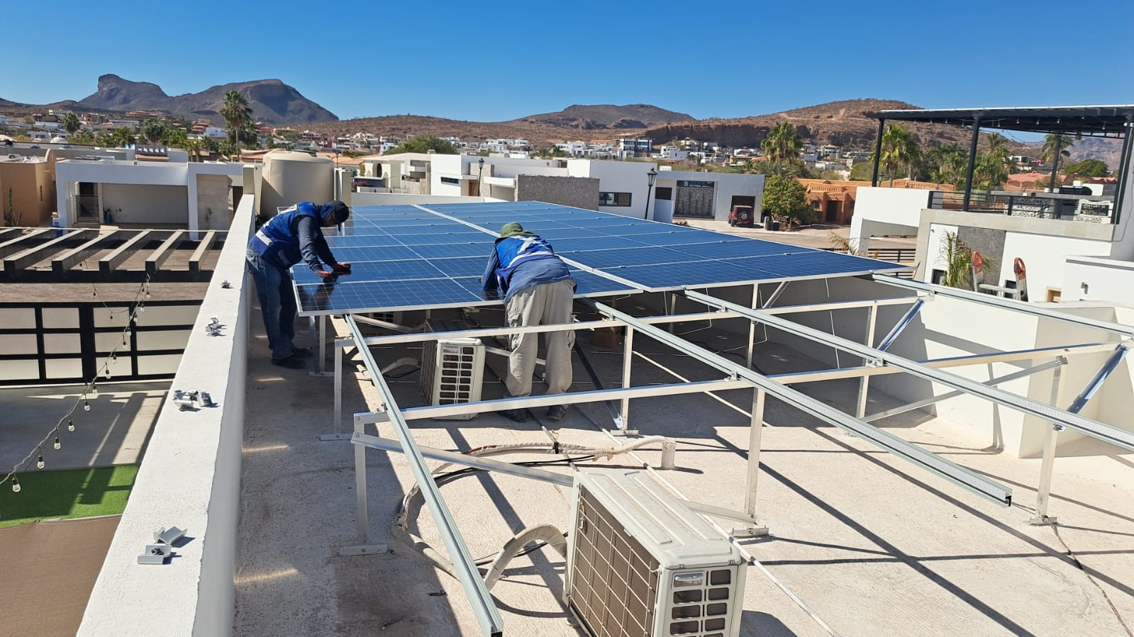 Workers installing solar panels on a rooftop, with a clear sky and residential area in the background.