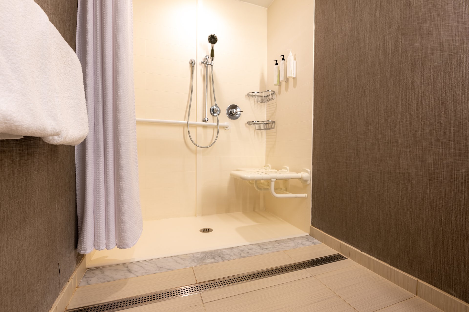 Wheelchair accessible hotel bathroom shower with tile floor and walls.