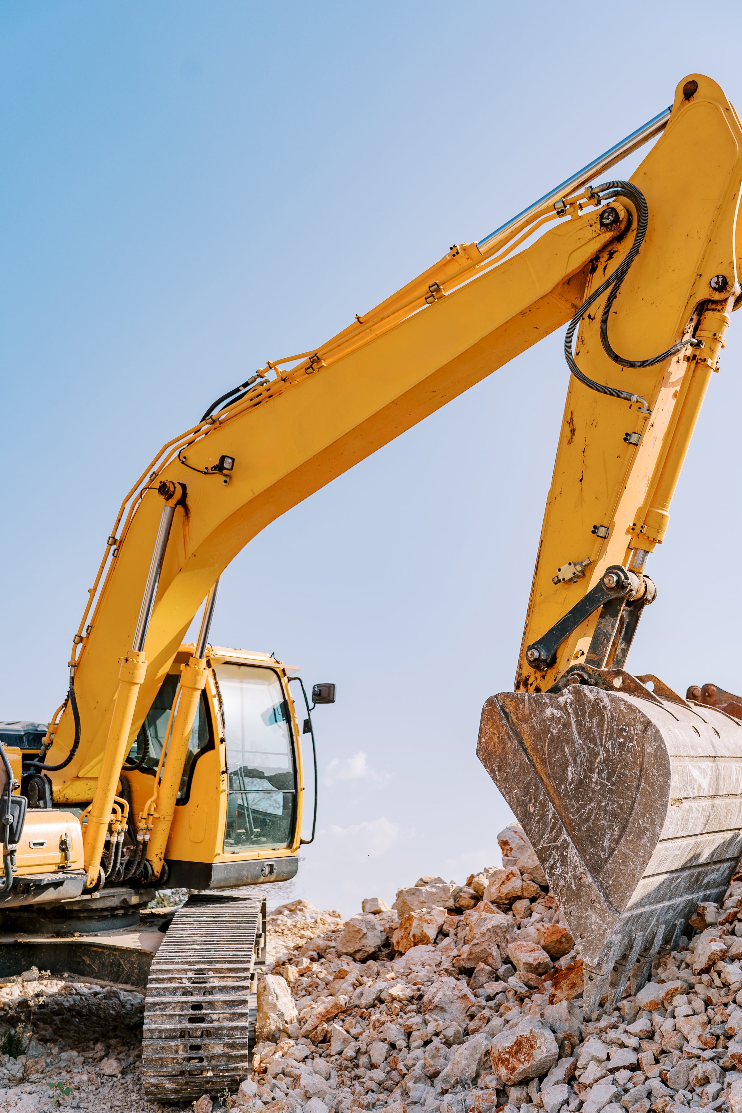 Yellow crawler excavator digs stones with a large bucket against a blue sky. High quality photo
