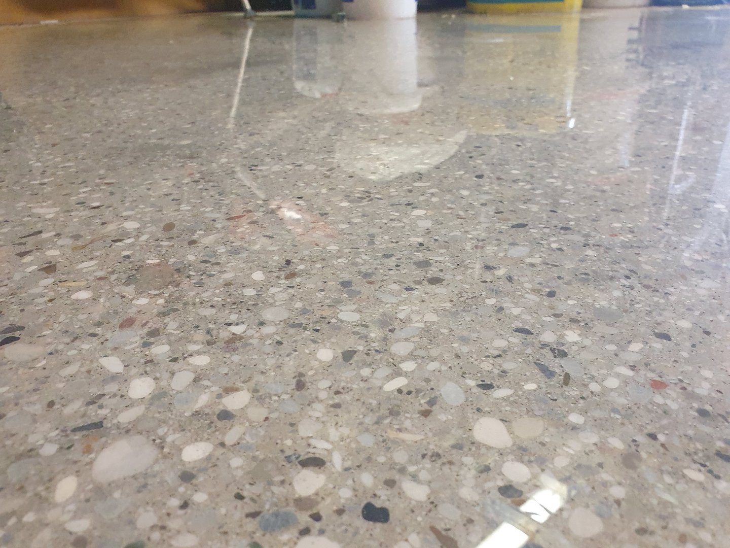 Close-up of a polished concrete floor with visible aggregate and a glossy finish, reflecting light and surrounding objects.