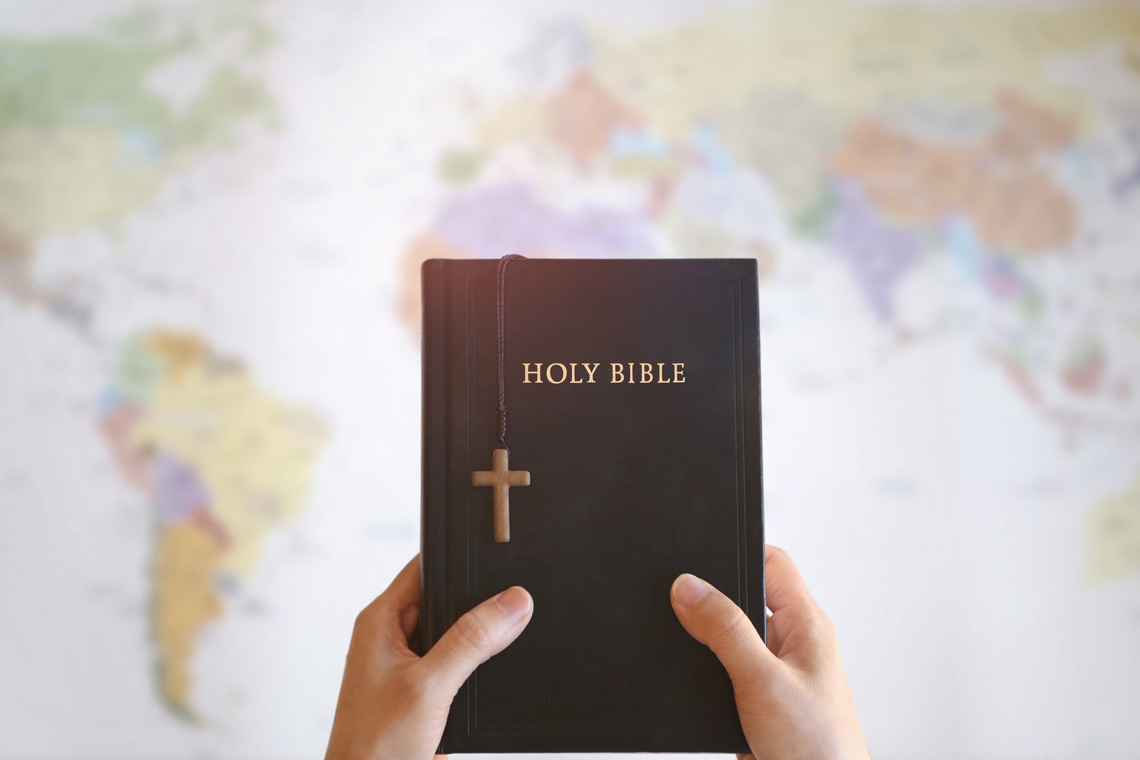 Christian holding the holy cross of Jesus Christ and the Bible in his hands and praying for missions, gospel and evangelism, world map background
