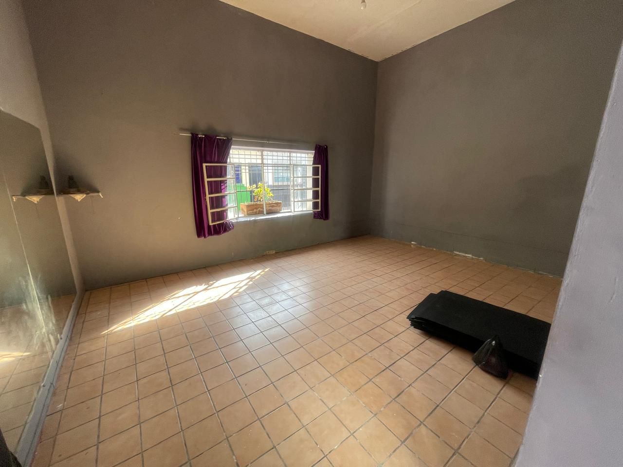 Empty room with a tiled floor, large window with purple curtains, and a small mattress on the floor.