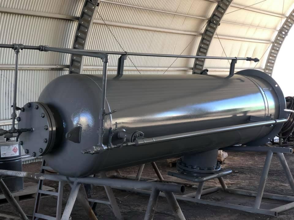 A large industrial metal tank inside a corrugated building, supported by a frame and connected to pipes.