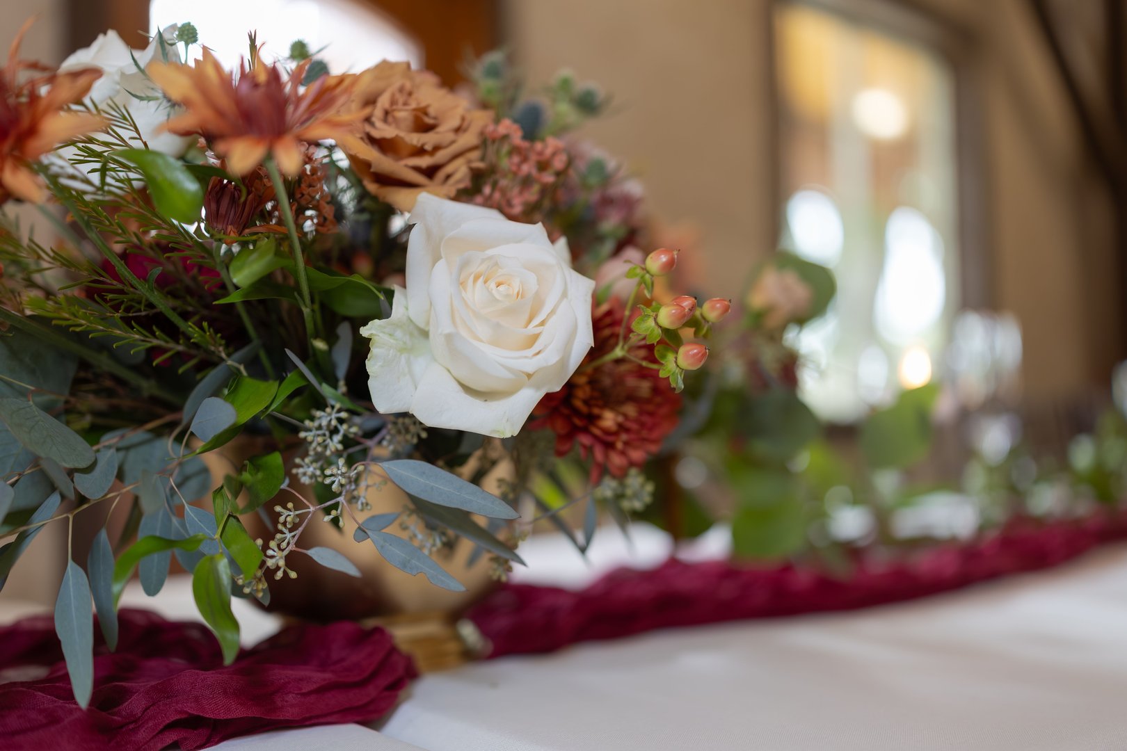 An elegant floral arrangement with white roses and autumn colors on a table setting, perfect for weddings or events.