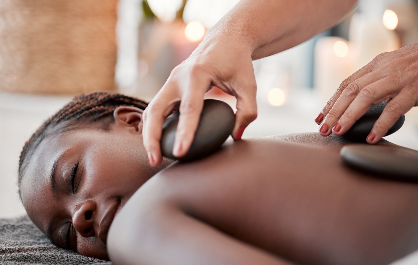 Black woman, hot stone massage, spa and hands of masseuse, holistic and wellness, therapy and treatment. Health, peace of mind and self care with zen, stress relief for people and back skin detox