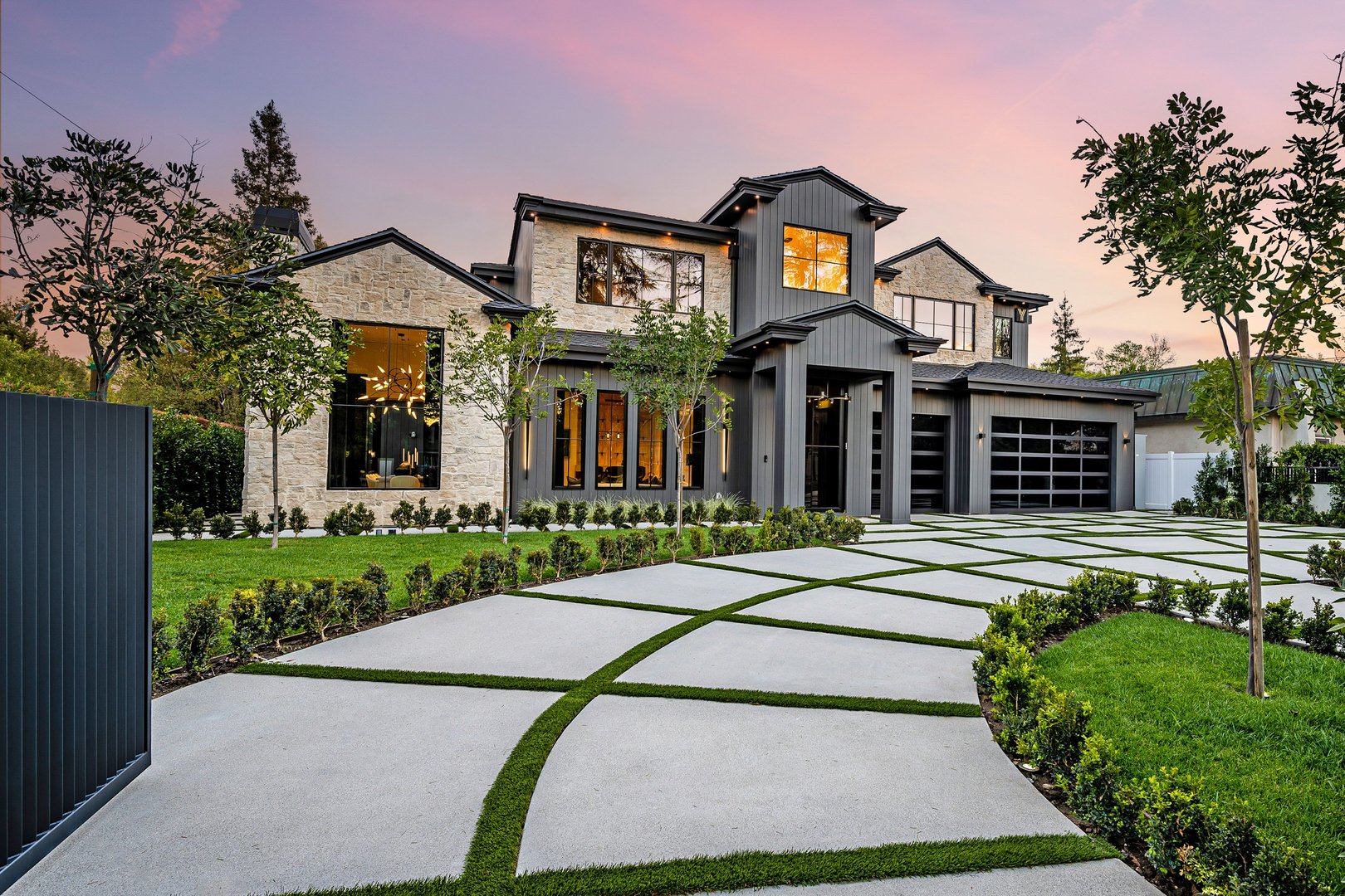 Modern luxury home exterior with a well-manicured lawn, geometric driveway, and sunset sky in the background.