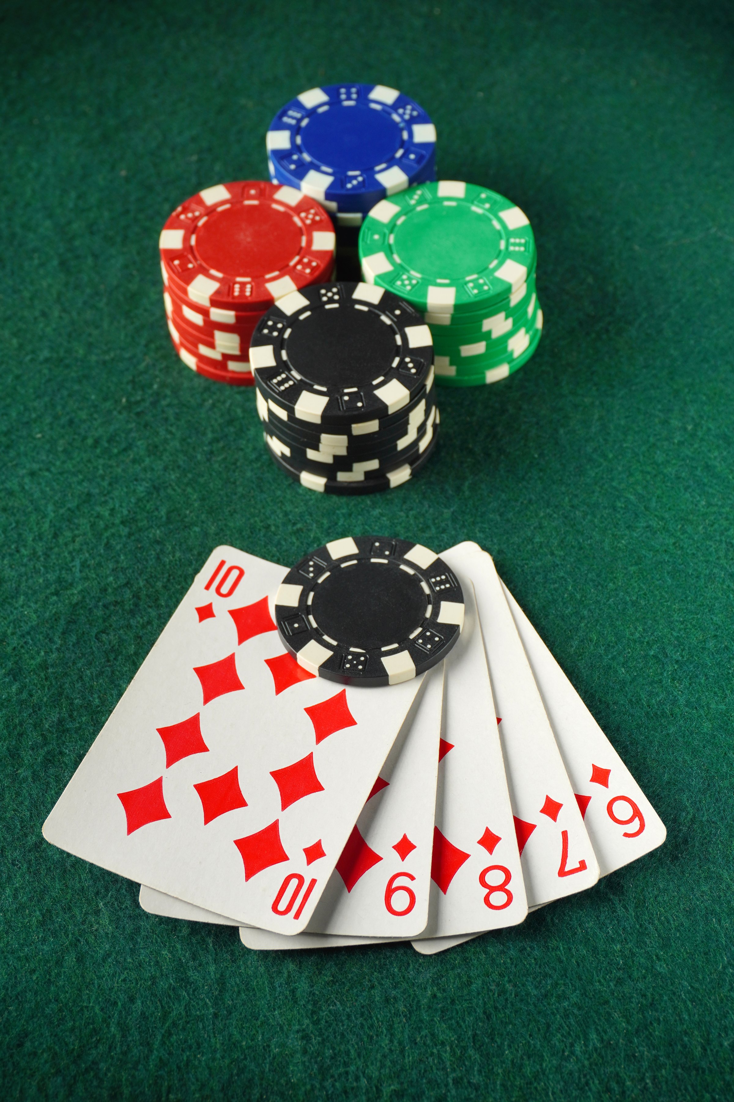 A hand reveals a winning poker hand consisting of straight flush cards numbered 6 to 10 with diamonds, alongside colorful poker chips stacked for a thrilling game night.