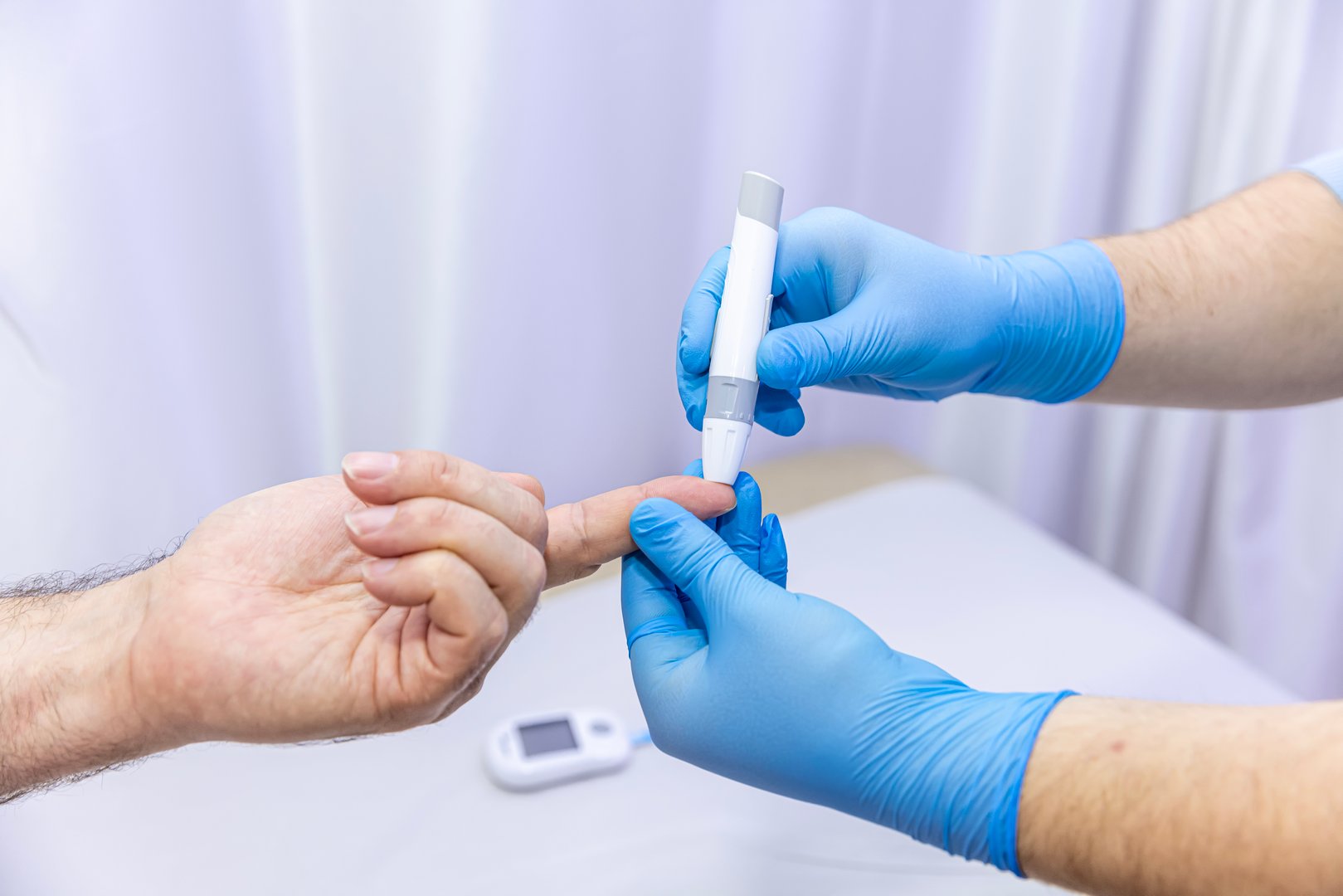Close-up of medical worker taking patient's blood sample with finger prick kit. Medical concept. Diabetes concept. Sugar in the blood. Health concept. Glucose meter in hand.