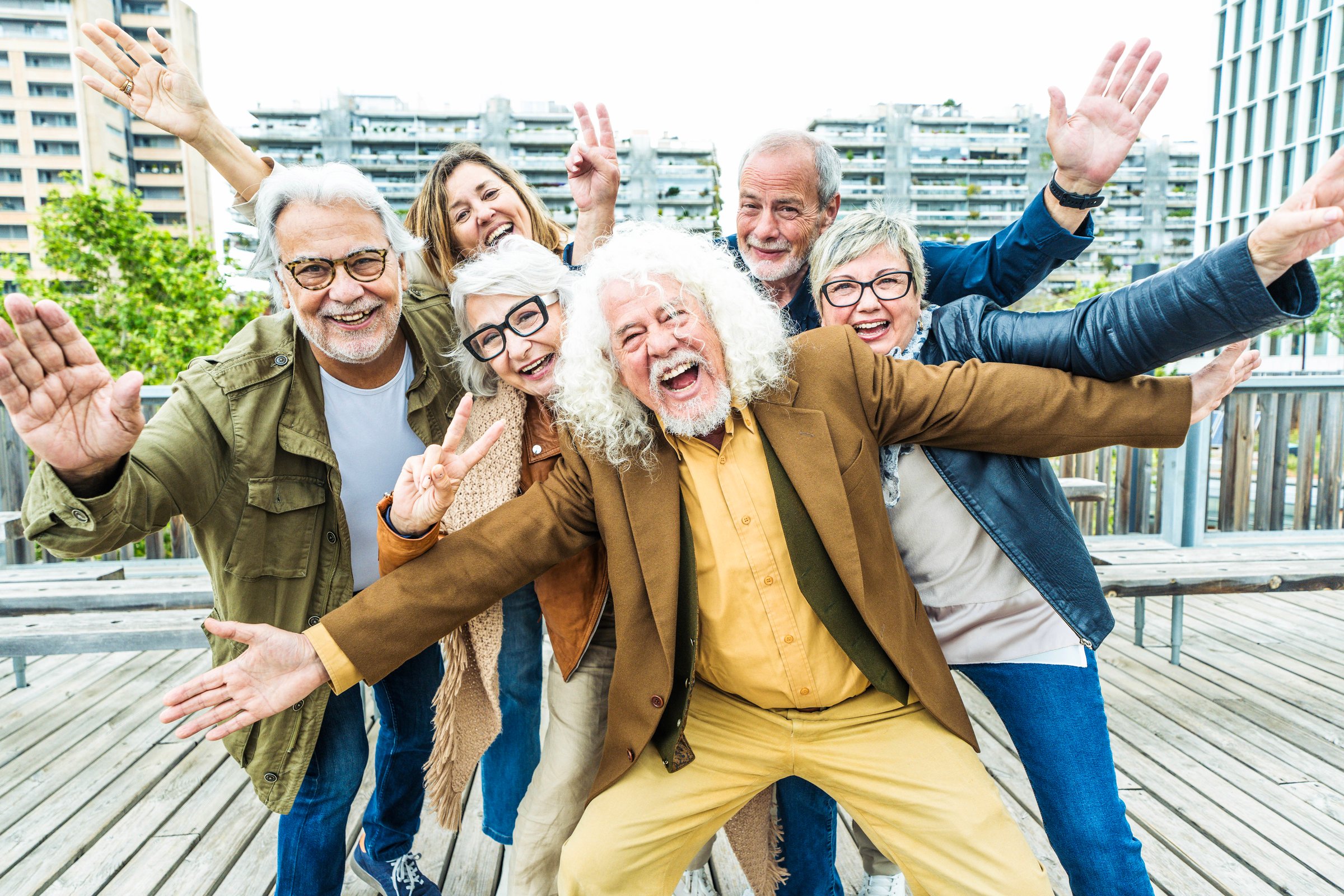 Happy group of senior people smiling together at camera outside - Delightful older friends enjoying day out walking on city street - Aged male and females pensioners hugging together outdoors