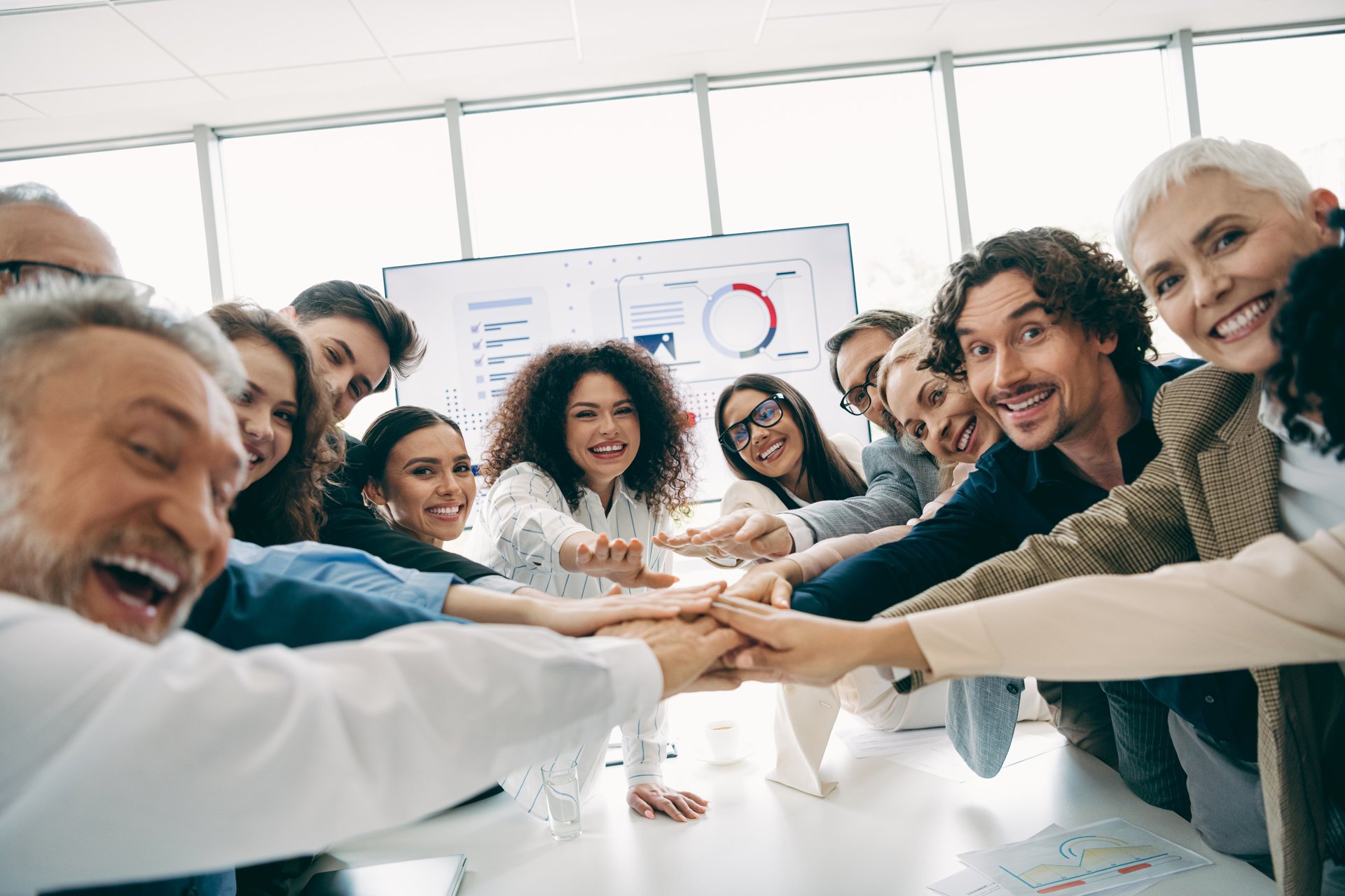 Diverse group of office professionals holds hands together symbolizing teamwork, unity, and partnership within a modern business workspace.