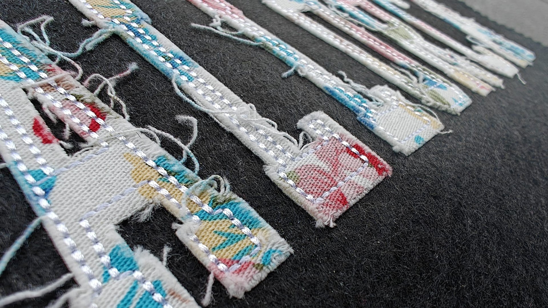 Close-up of fabric keys with colorful patterns and frayed edges sewn onto a dark background, arranged in a row.