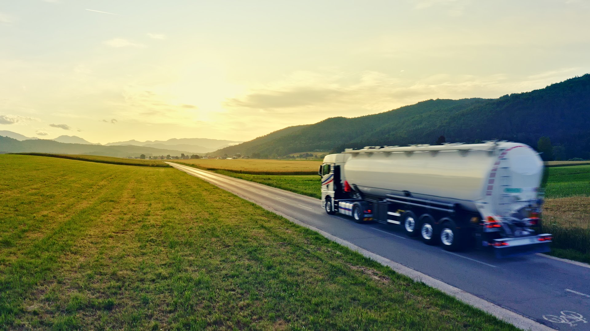 A tanker truck speeds down a rural road, symbolizing efficient cargo distribution and the interconnectedness of industries.