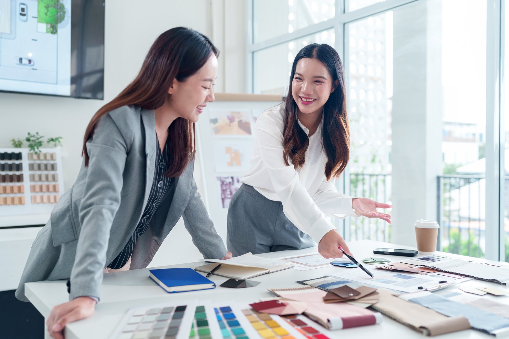Two Asian adult interior designers brainstorming ideas and planning architectural designs for renovation project in a modern studio with bright natural light at a meeting.