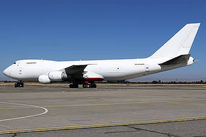 A white cargo airplane parked on an airport tarmac under clear blue skies.