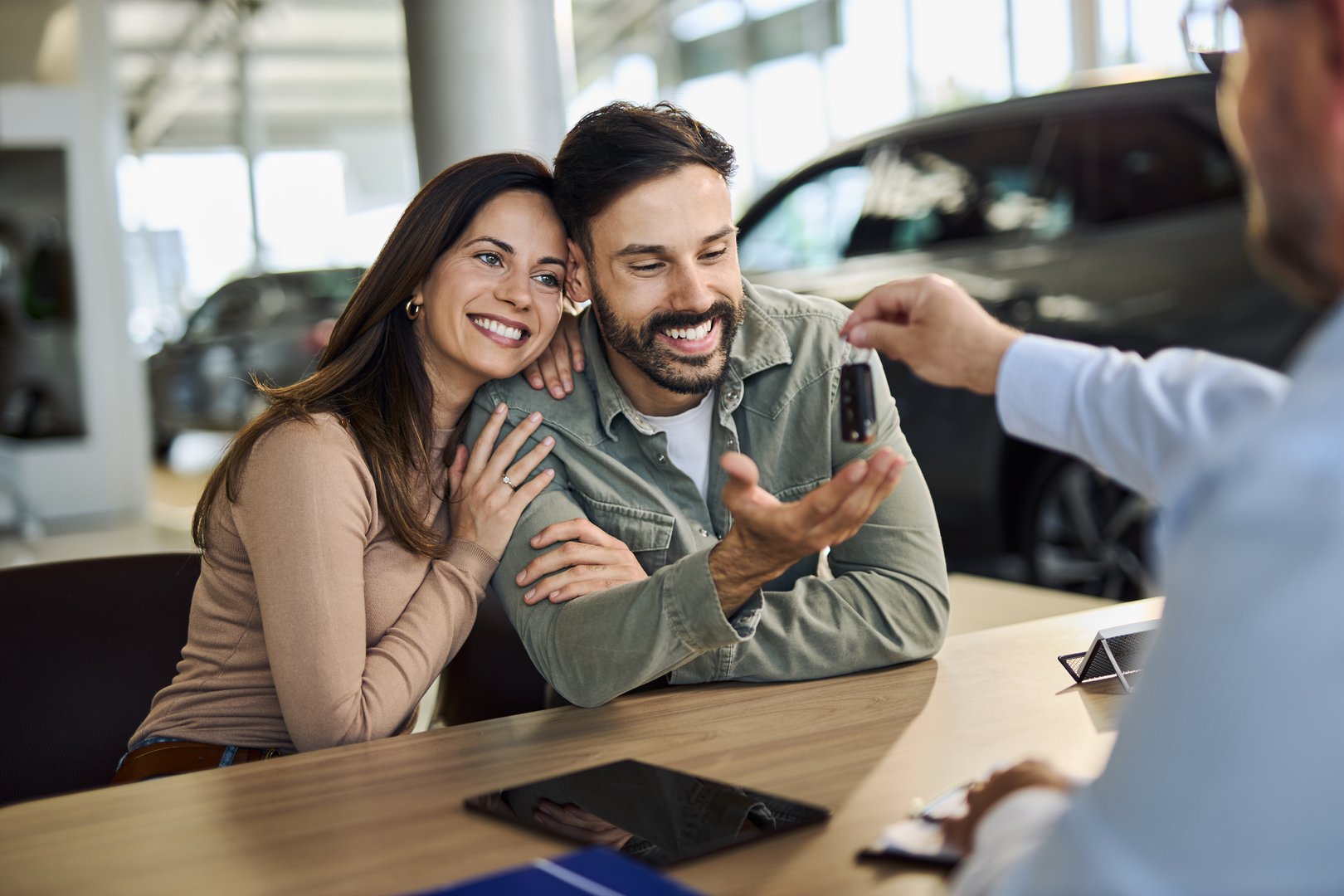 Happy couple receiving new car keys from a salesman on a meeting in showroom