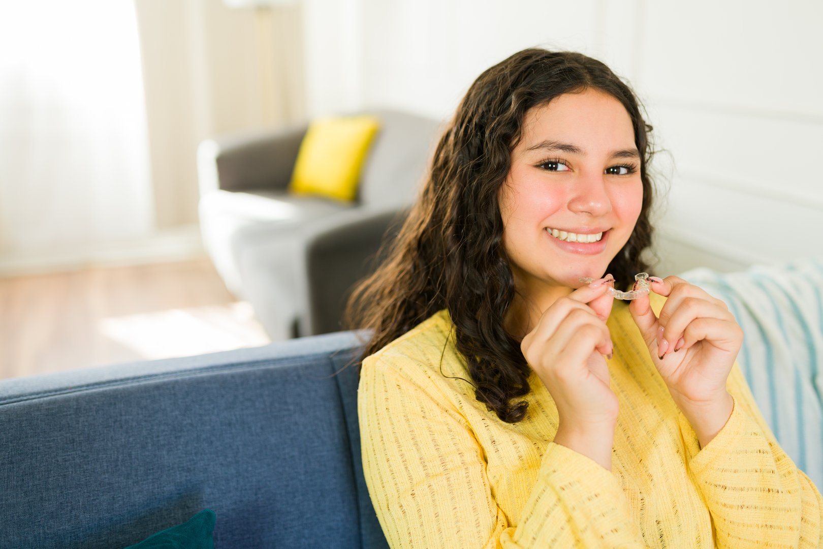 Portrait of a beautiful latin teenager holding her invisible braces and smiling while sitting on the sofa at home