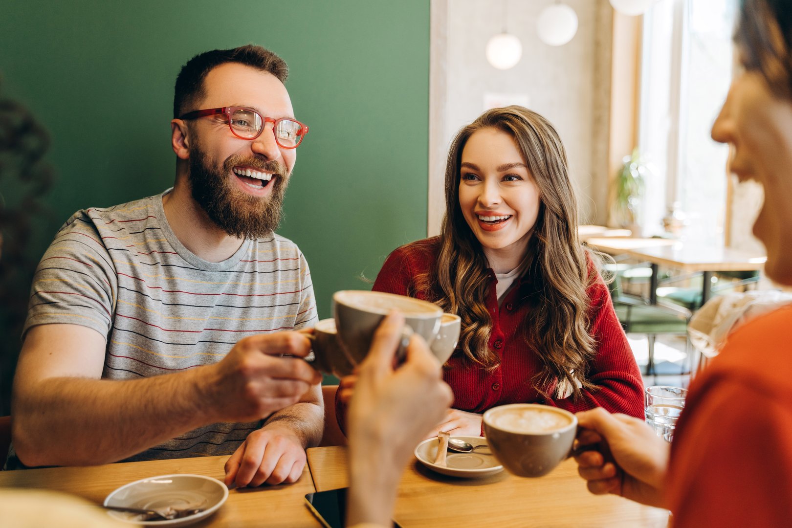 Cheerful friends enjoying a coffee break together, toasting their cappuccino cups and sharing laughter in a cozy cafe, creating warm memories and strengthening their bond. Relaxing concept