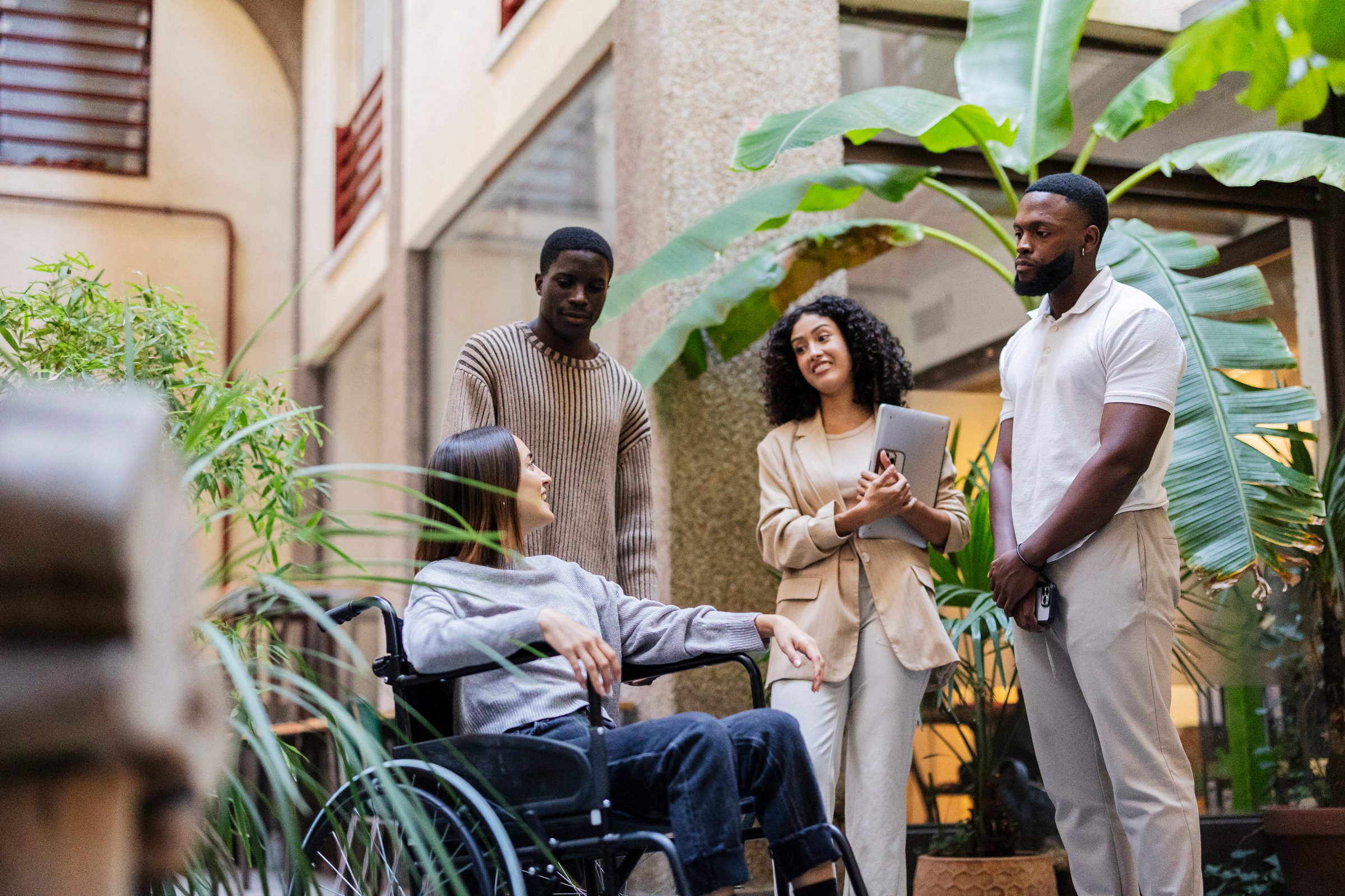 Multiracial businesspeople are discussing a project with a colleague in a wheelchair, promoting social inclusion and diversity in the workplace