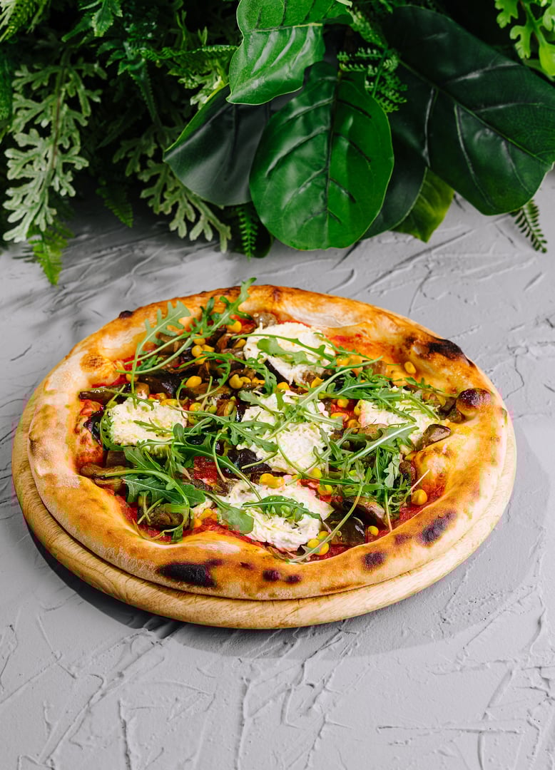 Gourmet veggie pizza with arugula and feta cheese on a textured surface