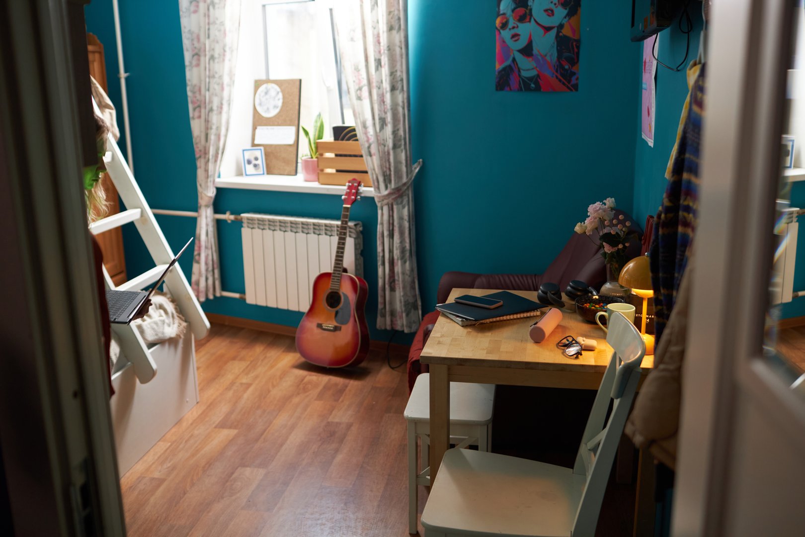 No people shot of modern girls dorm room interior with blue walls, decorated with colorful posters, bunk bed, table and chairs