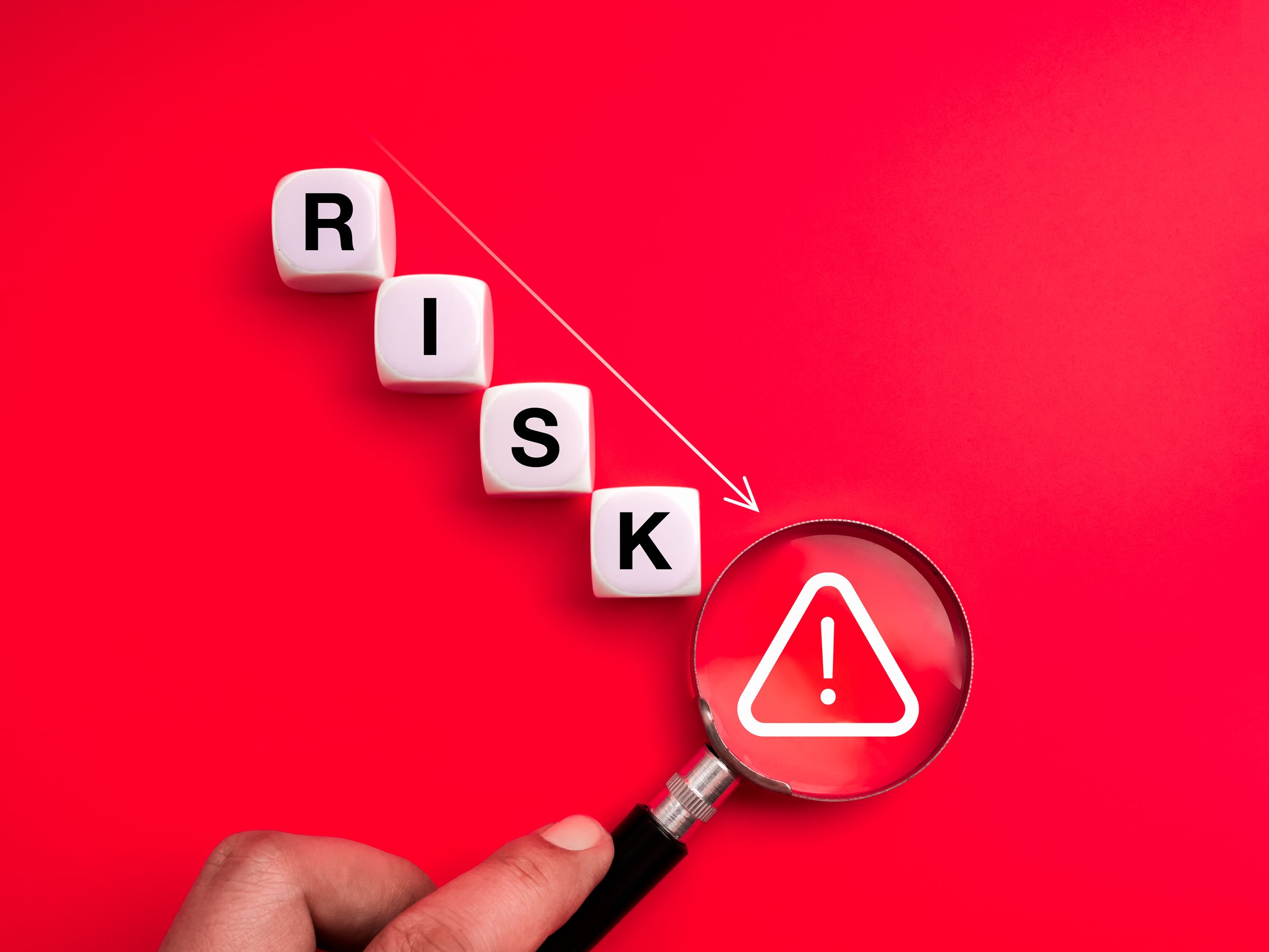 Weak cybersecurity and online scam concept with cubes down steps with RISK text and magnifying glass focus on warning symbol on red background. Fraud, data threats, downturn risk, and internet safety.