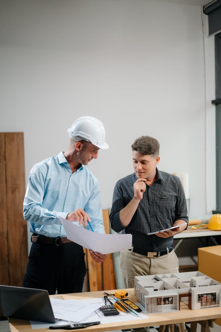 Two colleagues discussing data working and tablet, laptop with architectural project at construction site at desk in office