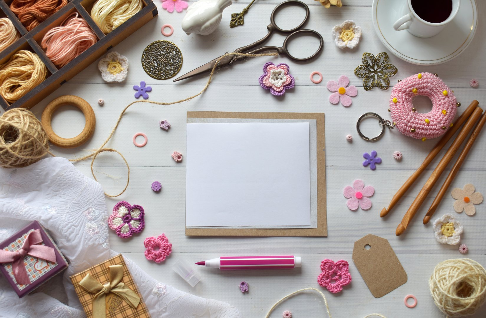 Handmade DIY workspace flat lay with yarn threads scissors crochet hooks and colorful accessories on a white wooden surface perfect for artisan craft and hobby projects