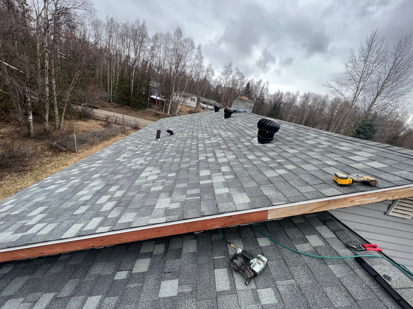 Roofing project Anchorage Alaska - newly installed shingles ventilation pipes and tools on sloped roof reflecting quality workmanship