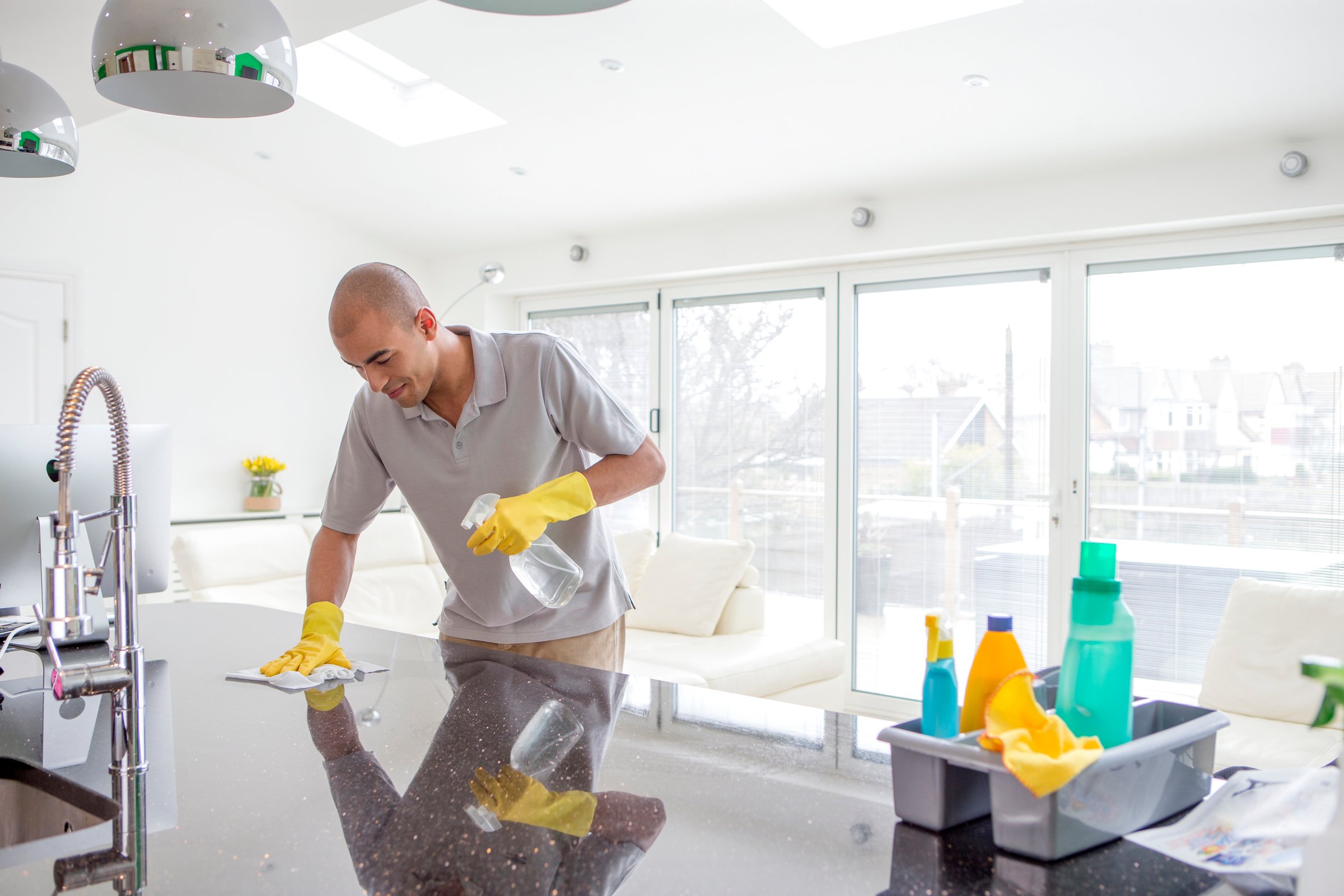 Shot of a young mixed race man cleaning a kitchen top. The kitchen is open planned and spacious.